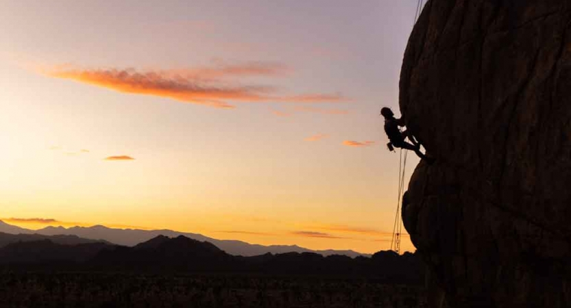 The silhouette of a person rock climbing appears against the gentle colors of the sky behind them. 